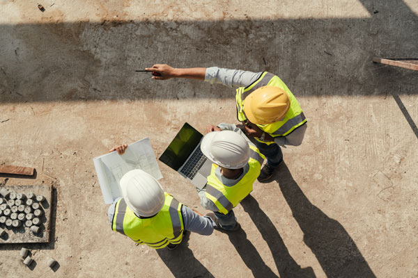 Photo taken from above of three men in high vis and hard hats, one of them is pointing to something in the distance