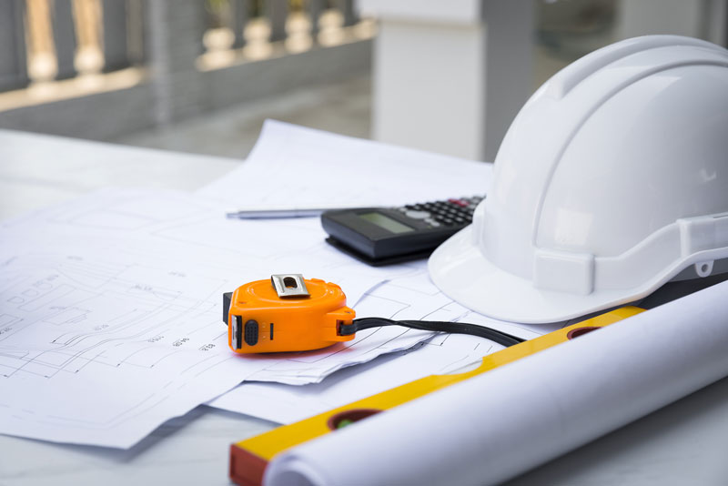 Hard hat on a table, next to it is a tape measure, paper, calculator, spirit level